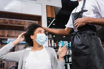 African american woman in protective mask pointing at hairstylist