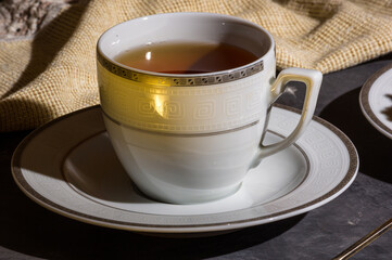 Cup of hot black tea on a white saucer and a linen napkin, black background, hard light, photo in a low key.