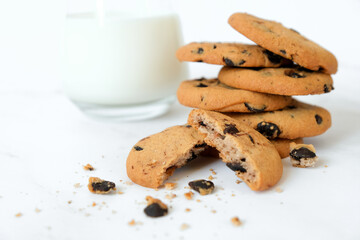 Stack of homemade chocolate chip cookies and glass of milk on marble background. Recipe of traditional pastry for tea, freshly baked cookies with pieces of chocolate. Selective focus.