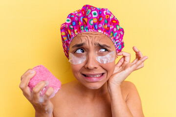 Young mixed race woman taking a bath holding a sponge bath with a dark circle patches isolated covering ears with hands.