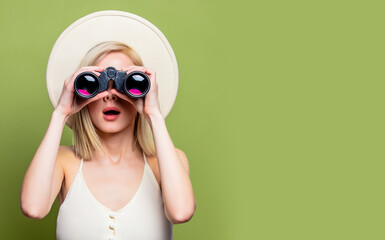 Beautiful blonde girl in a white hat and dress with binoculars