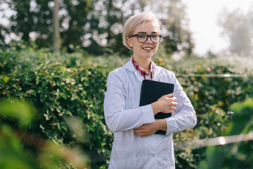 Portrait of young woman agronomist at plantation. Worker with tablet smiles and looks into camera.