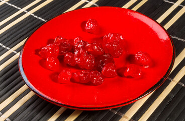 Sweet dried cherries in a red saucer on a bamboo mat, close-up.