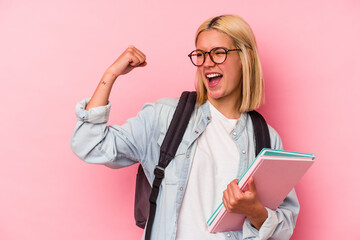 Young venezuelan student woman isolated on pink background raising fist after a victory, winner...