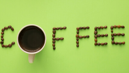 A cup of coffeeas a letter in the name of coffee  made from beans on a green background