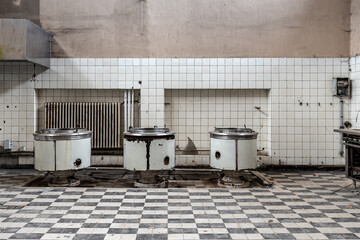 Abandoned large kitchen with 3 large cooking pots and checkerboard pattern tiles
