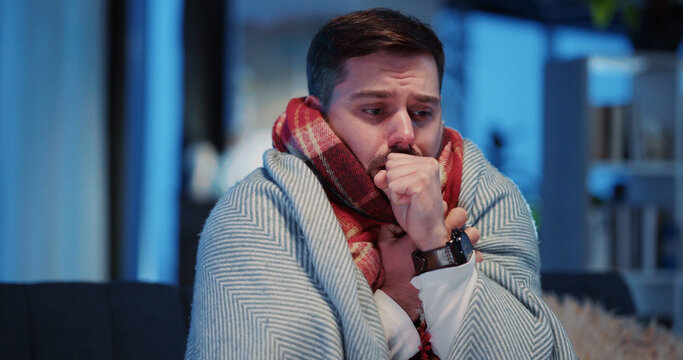 People, healthcare, pandemic concept. Young sick caucasian businessman staying home in the evening warming up in blanket sneezing allergy feel badly.