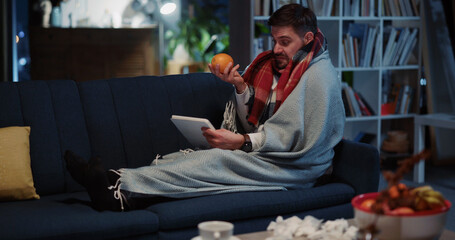 Bearded ill businessman staying home videochatting on laptop call with mother showing orange eating healthy foods to recover sickness. Communications.