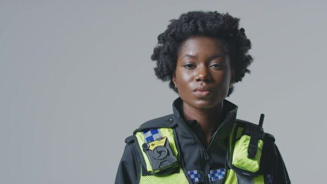Serious young female police office wearing uniform in front of plain studio background - shot in slow motion