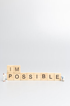 Miniature  people worker team on impossible word in wooden alphabet letters with prefix un crossed out, leaving the word possible