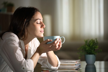 Relaxed woman smelling coffee in the night at home