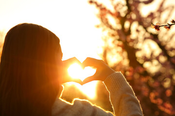 Woman hands making heart shape at sunset