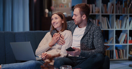 Affectionate young caucasian couple of girlfriend and boyfriend lying on couch together using mobile phone watching videos communication online.