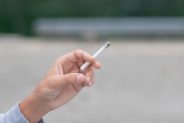 Close up of man hand holding a lit up cigarette. Selective focus, space for copy. Bad habits, health issues concept.