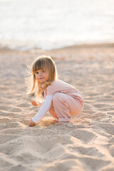 Pretty little child 2-3 year old playing at beach over sea at background in sun light outdoors. Small kid wearing summer clothes outside. Vacation season. Childhood. Looking at camera.