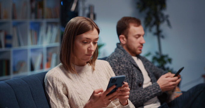 Argued Young Angry Caucasian Couple Making Conflict Agruing wih Each Other Using Mobile Phones Sitting Separately in Living Room. Quarrel.