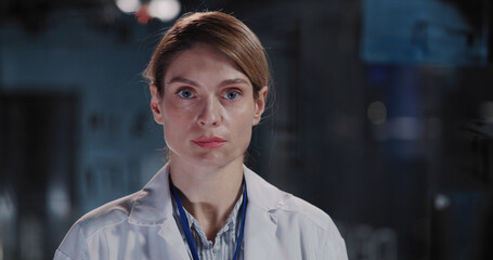 Indoor portrait of cheerful blonde young doctor in laboratory suit smiling for camera working with chemical equipment inside modern lab office.