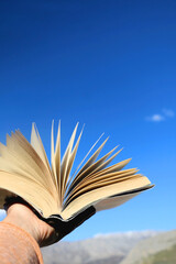 Hand holding open book up to the sky. Selective focus.