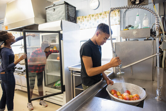 Teen boy volunteer washing apples at sink in community center kitchen