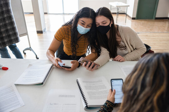 Happy teen girl friends in face masks taking selfie in classroom