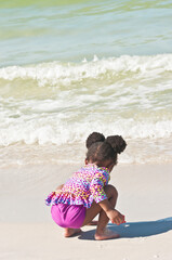 back view, medium distance of a young, black, girl in a colorful bathing suit, playing on the shoreline of a tropical, sandy beach, on gulf of Mexico