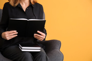 Obraz premium Woman with books sitting in armchair on color background