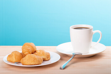 delicious coffee with croissant on wooden table and blue background