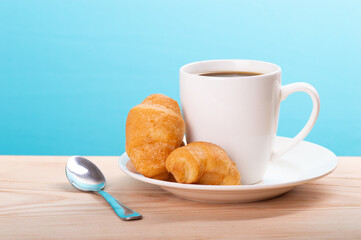 delicious coffee with croissant on wooden table and blue background