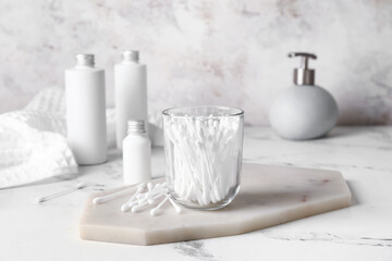 Glass with cotton swabs and cosmetic products on table in bathroom