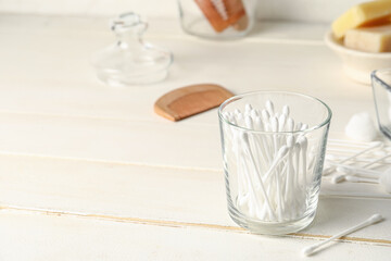 Glass with cotton swabs and bath supplies on table in bathroom