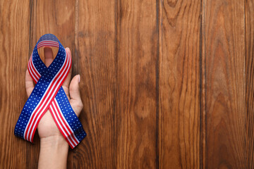 Female hand with ribbon in colors of USA flag on wooden background