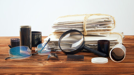 A stack of old photographs, glasses, a magnifying glass and negatives on a wooden table.
