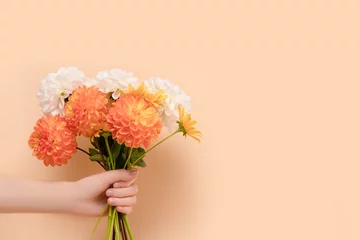 Deurstickers Female hand hold bouquet of dahlia flowers in front of beige background. Woman giving gift for 8 March or Mothers Day. © rorygezfresh
