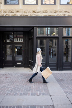 Woman in face mask walking with shopping bags along city storefront