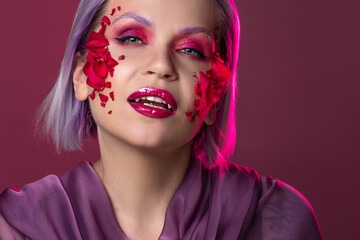 stylish and bright young woman with colored makeup and flower petals on her face
