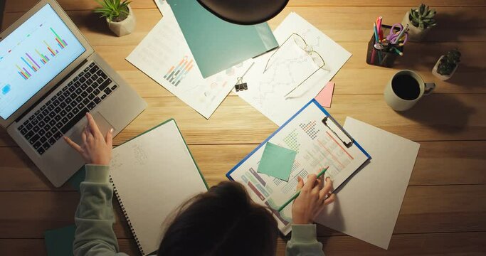 Young female freelancer working at home late in evening, top view
