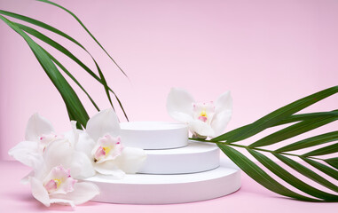 Obraz na płótnie Canvas White geometric shapes podium for product display on pink background with orchid flowers and palm leaves. Monochrome stage, stand for product promotion in minimal style. Copy space for your design. 