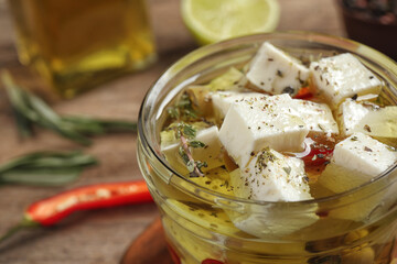 Glass jar of marinated feta cheese on wooden table, closeup