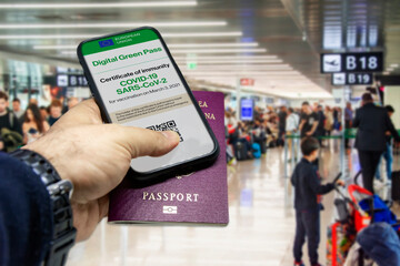 Fototapeta na wymiar Male hand holding a phone with the European Union vaccination certificate on the screen and a traditional passport inside an airport