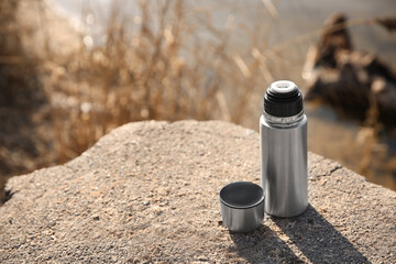 Modern silver thermos on stone near river