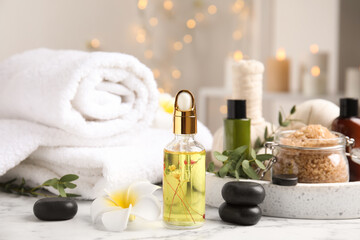 Fototapeta na wymiar Beautiful spa composition with essential oil and plumeria flower on white marble table against blurred lights