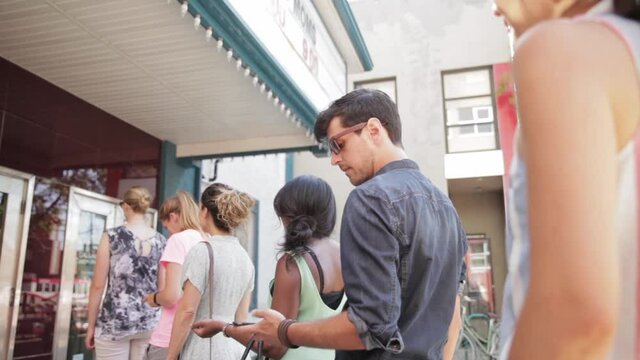 Man With Smart Phone Waiting In Queue Outside Movie Theater