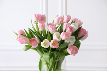 Beautiful bouquet of tulips in glass vase against white wall