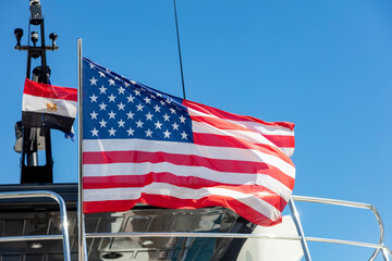 USA flag on pole on ferry's stern. Ongoing cruise to islands. Blue sky background