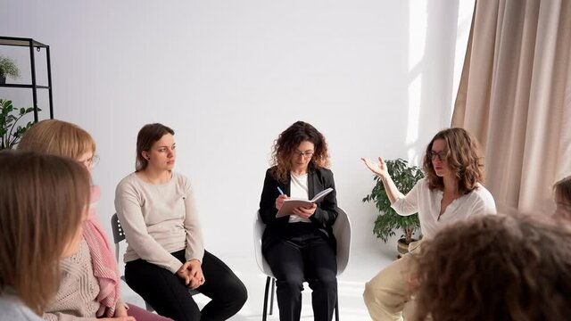 Psychological group meeting women under the guidance of a psychologist. Women talk, psychologist makes notes in notebook