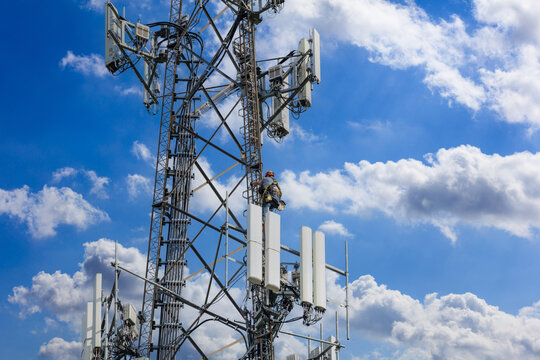 Telecom maintenance. Man climber on tower against blue cloudy sky background.