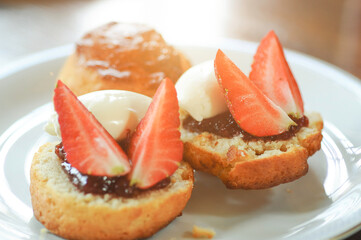 Close up strawberry scones with jam and whipped cream in white plate.