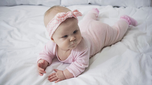 baby girl in headband with bow lying on bed.