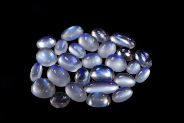 Natural blue sheen adularia moonstones oval cabochone polished gemstones lot. Milky crystal massif with blue shine. Feldspar mineral group earth mined stones. Black background.