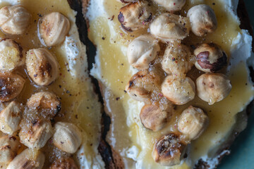 Two bread toast with cream cheese, roasted hazelnuts, honey, pepper and salt, close up, top view